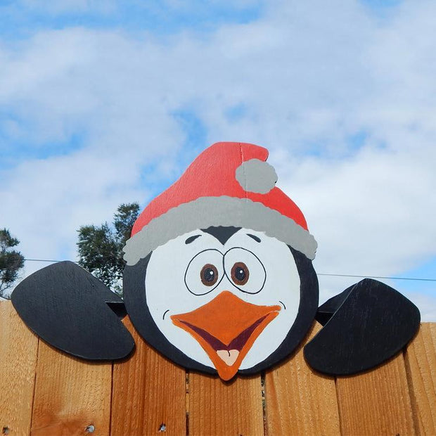 Christmas themed fence decoration featuring a cheerful penguin wearing a Santa hat outdoors
