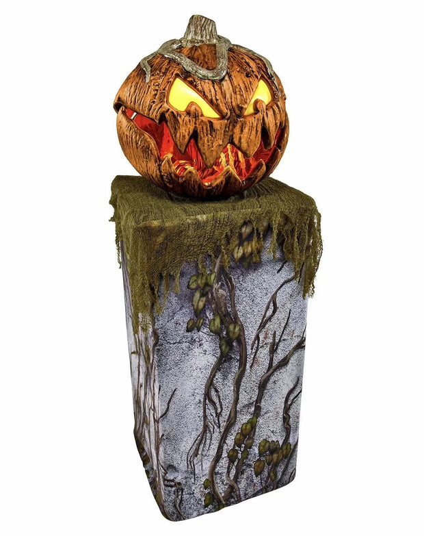 Halloween pumpkin lighting decoration with glowing eyes and mouth on a decorative pedestal for outdoor garden party